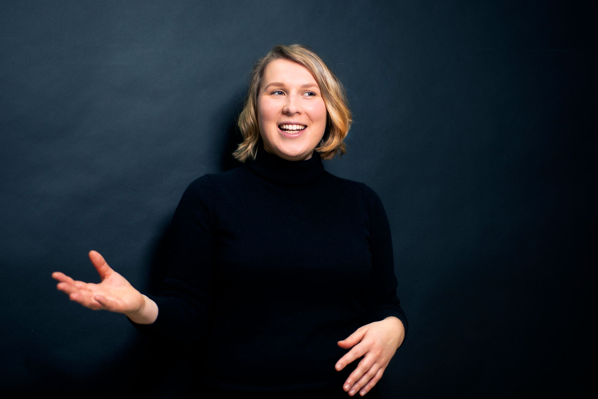 EIn Portraitfoto von Denise Loop im schwarzen Rollkragenpullover. Sie gestikuliert im Gespräch mit ihren Händen.